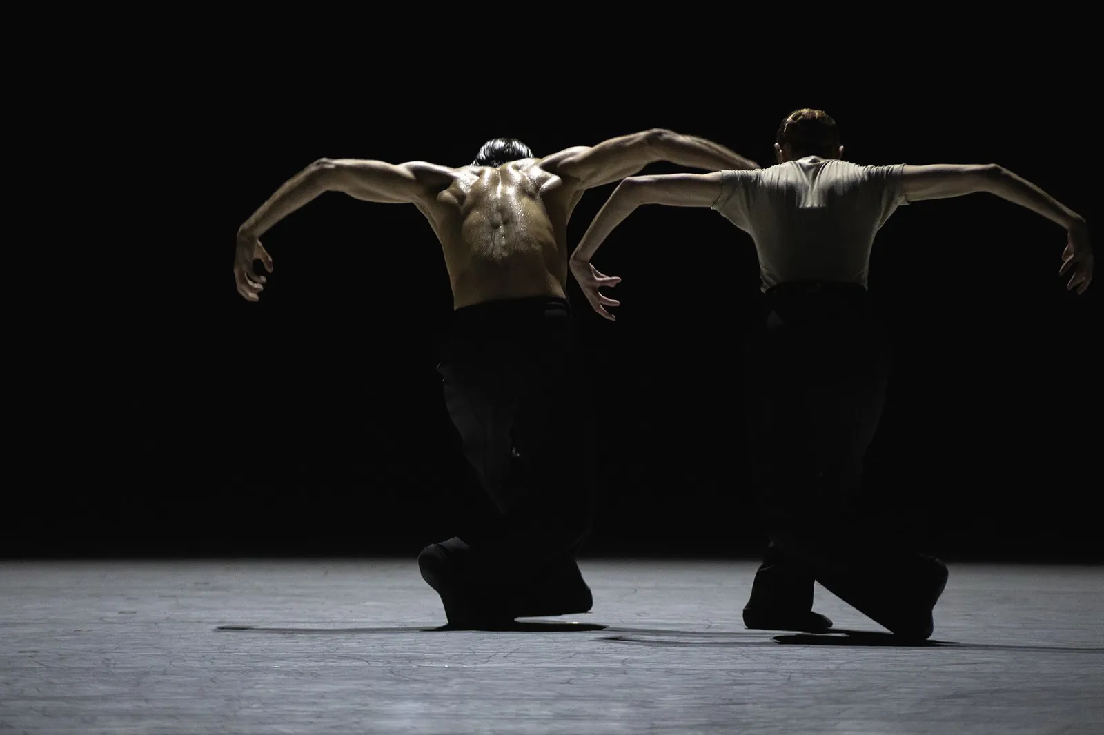 Two dancers performing side by side under a spotlight